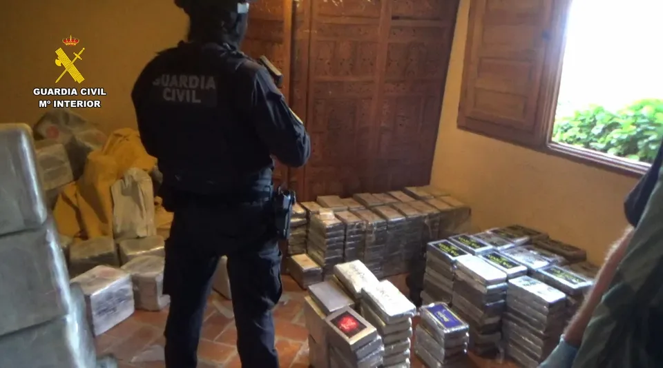 Un agente de la Guardia Civil observa numerosos paquetes de droga apilados en una habitación durante una operación policial.