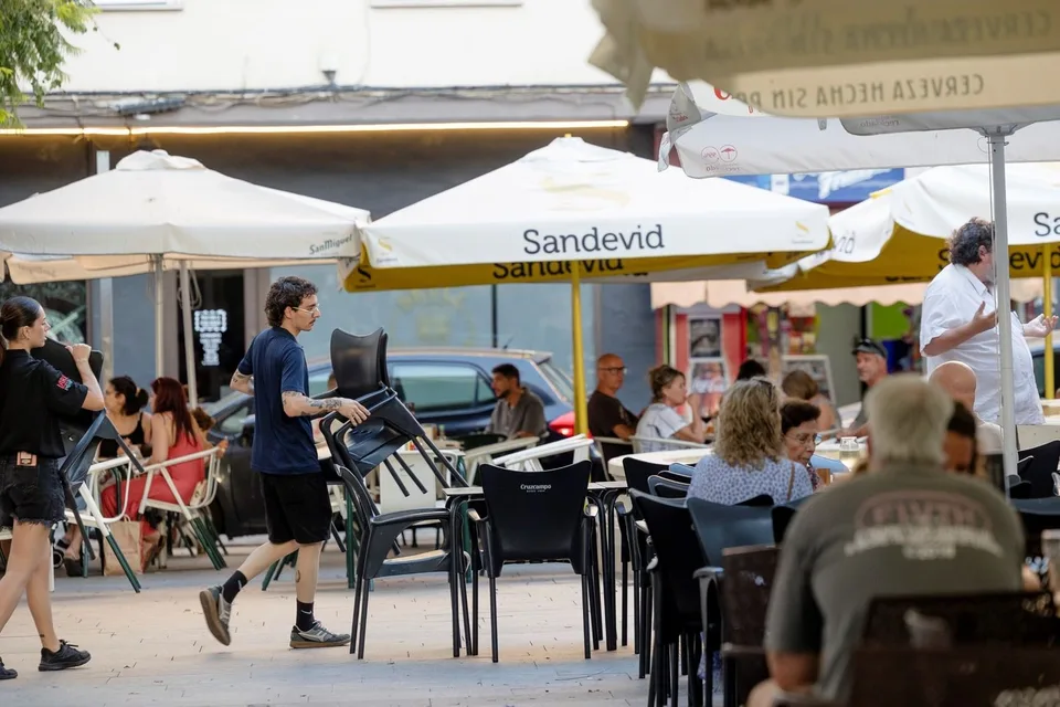 Dos camareros preparando mesas y sillas en una terraza de Cádiz, fotografía documental de trabajadores de la hostelería vinculada a la EPA provincial.