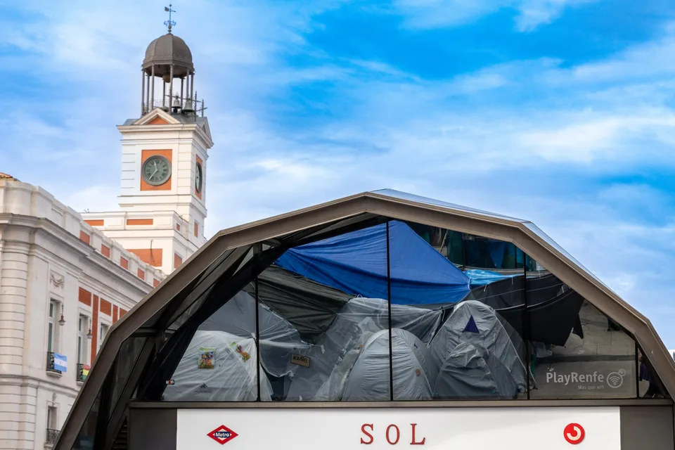 Reflejos de las tiendas de la acampada por vivienda en la estación de Sol, Madrid, con la Casa de Correos al fondo, el 11 de octubre de 2026.