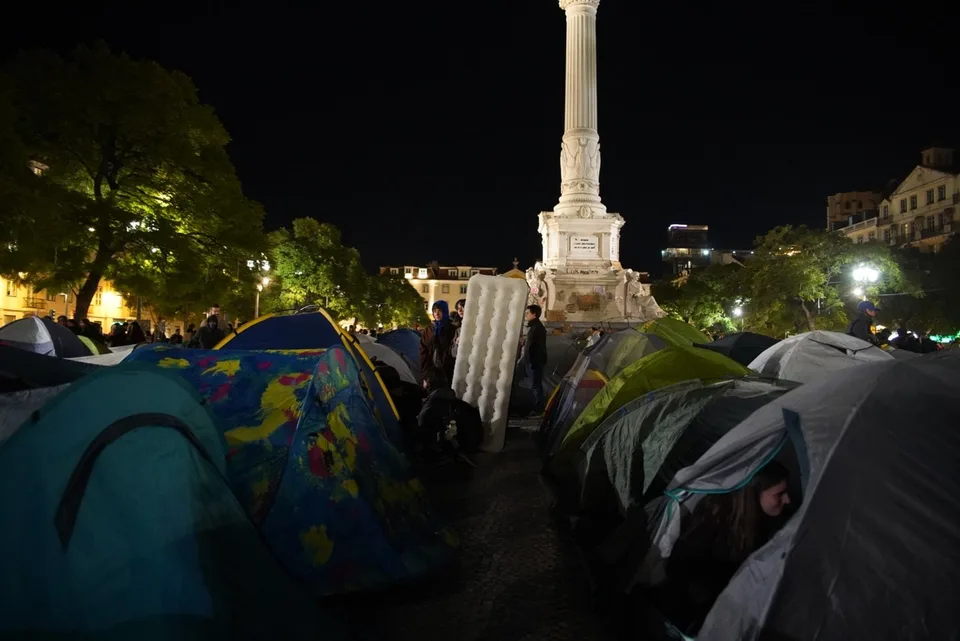 Fotografía real de la acampada de protesta por la vivienda en Rossio, Lisboa, la noche del 24 al 25 de octubre de 2026.