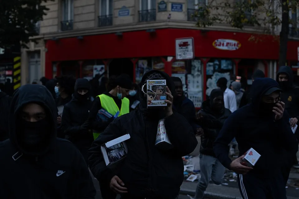 Personas con el rostro cubierto transportan cajas de figuras coleccionables sustraídas de una tienda durante los disturbios de París del 17 de octubre de 2026.