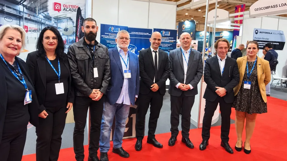 Ocho profesionales posan en el espacio de HSI Intelligence durante SEGUREX 2026 en la Feira Internacional de Lisboa, frente a paneles de seguridad e inteligencia y otros expositores de la feria.
