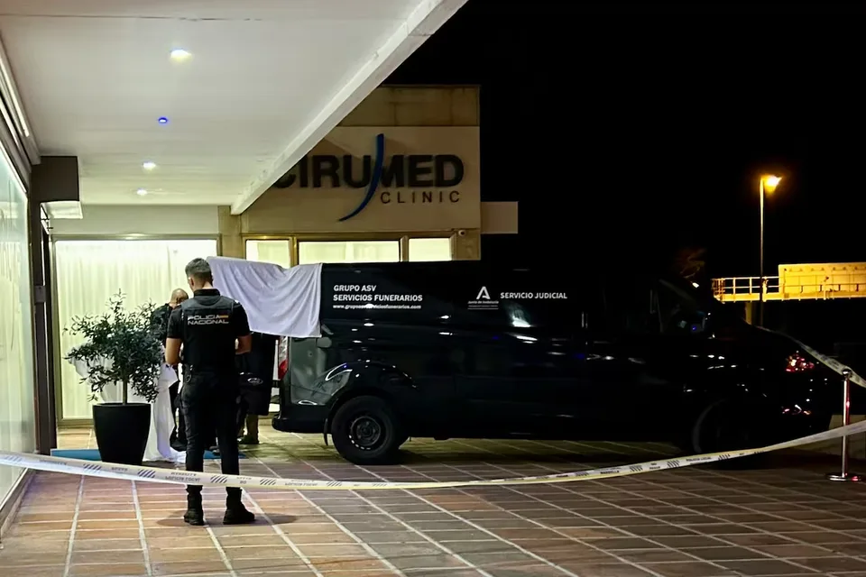 Un agente de Policía Nacional y un vehículo de servicio judicial en el exterior nocturno de la clínica Cirumed en Marbella.