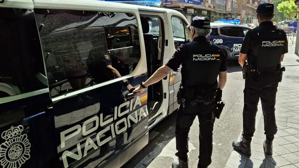 Dos agentes de la Policía Nacional junto a un vehículo policial estacionado en una calle urbana.