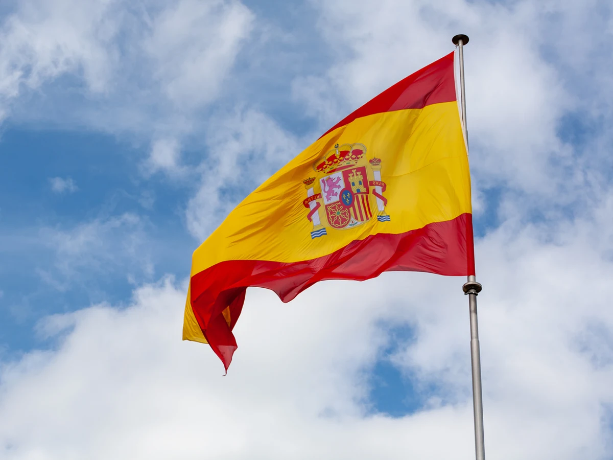 Bandera de España ondeando en un mástil bajo un cielo parcialmente nublado.