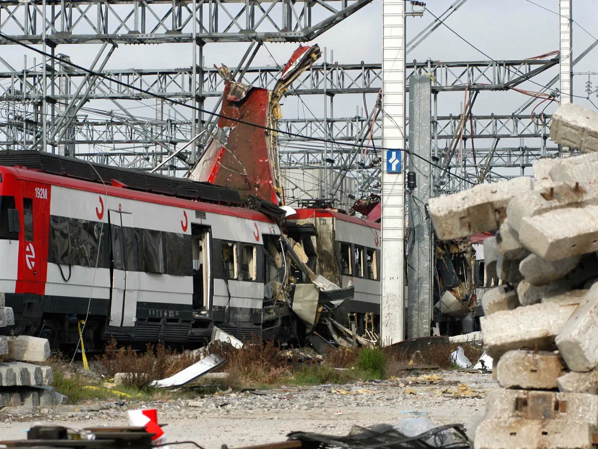 Tren de Cercanías destrozado tras los atentados del 11-M de 2004 en Madrid, mientras los servicios de emergencia trabajan junto a las vías.
